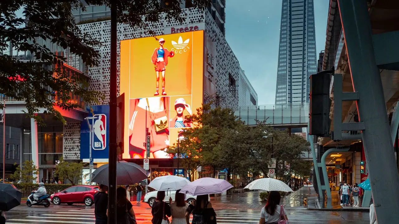 Personas con paraguas en una calle iluminada por pantallas